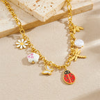 Gold-tone ladybug charm bracelet with flower and pearl charms; chained bracelet on light background