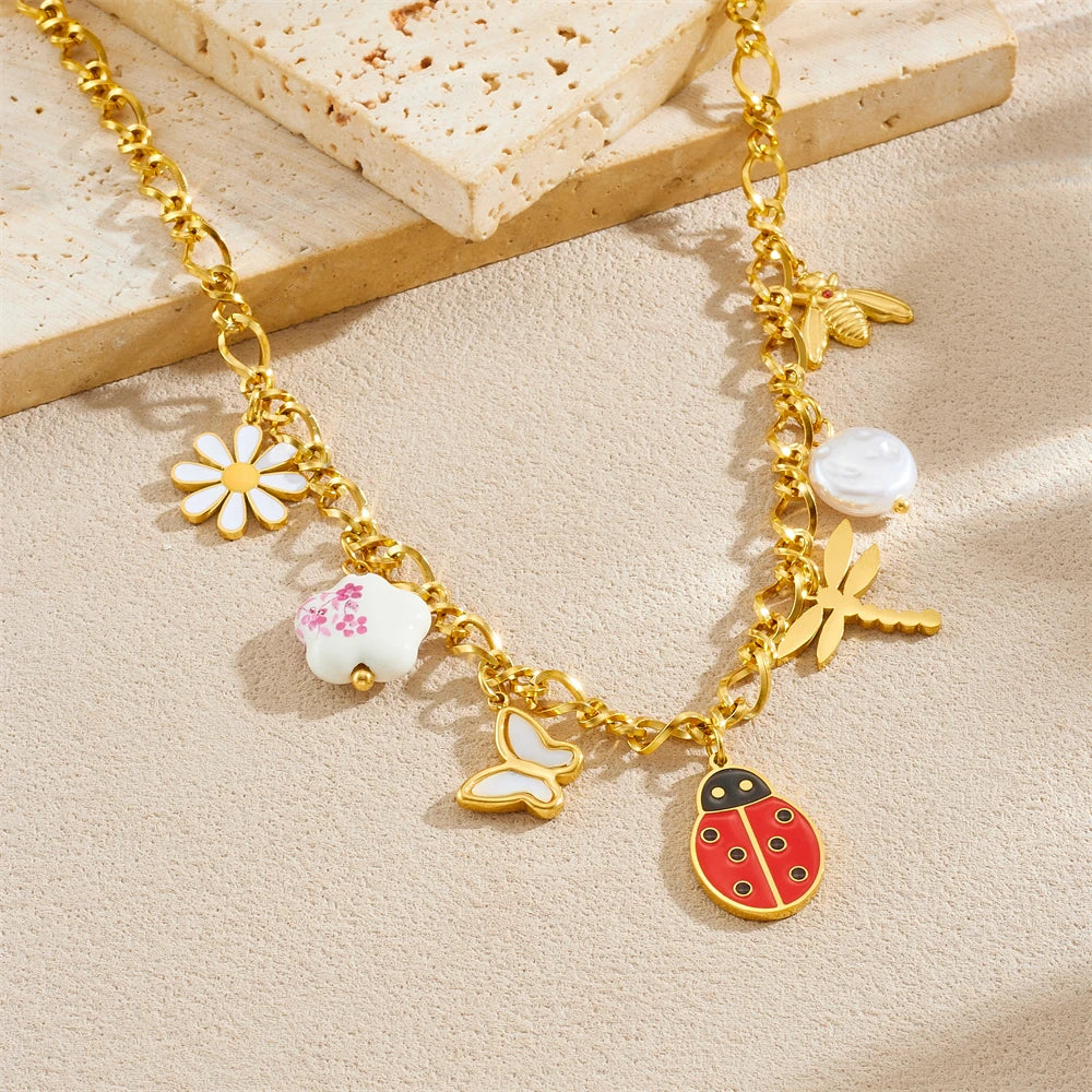 Gold-tone ladybug charm bracelet with flower and pearl charms; chained bracelet on light background