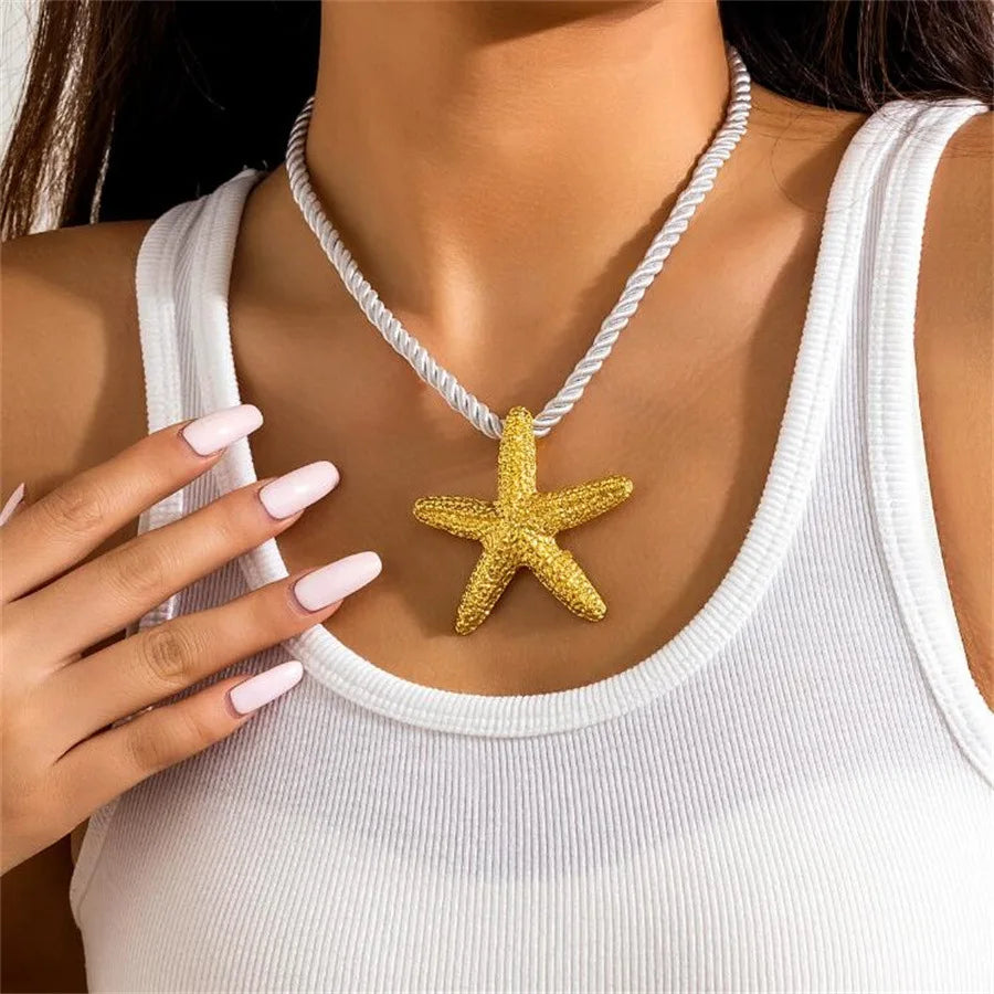 Gold starfish pendant necklace on a person wearing a white tank top.