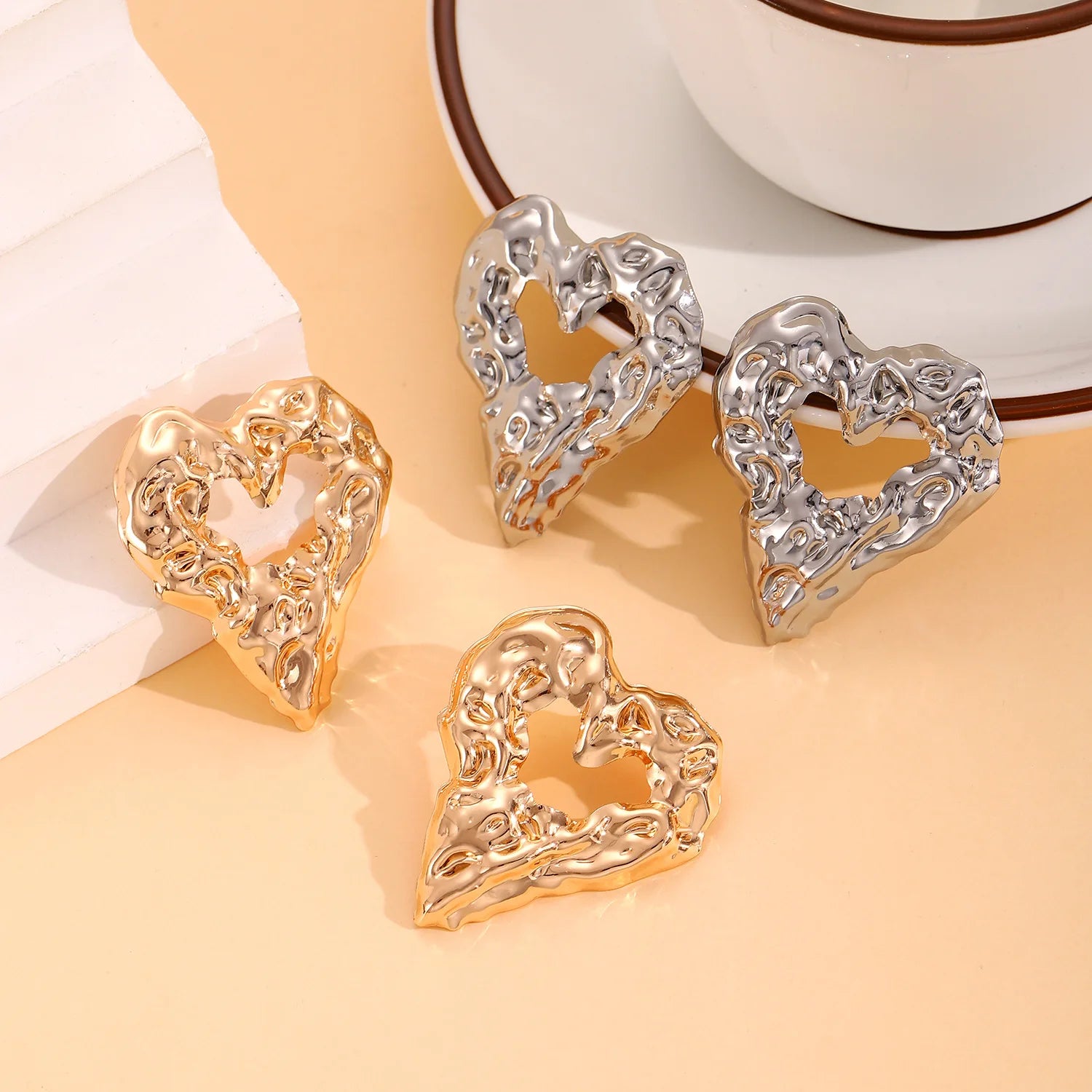 Heart-shaped drop earrings in gold and silver with ornate raised texture