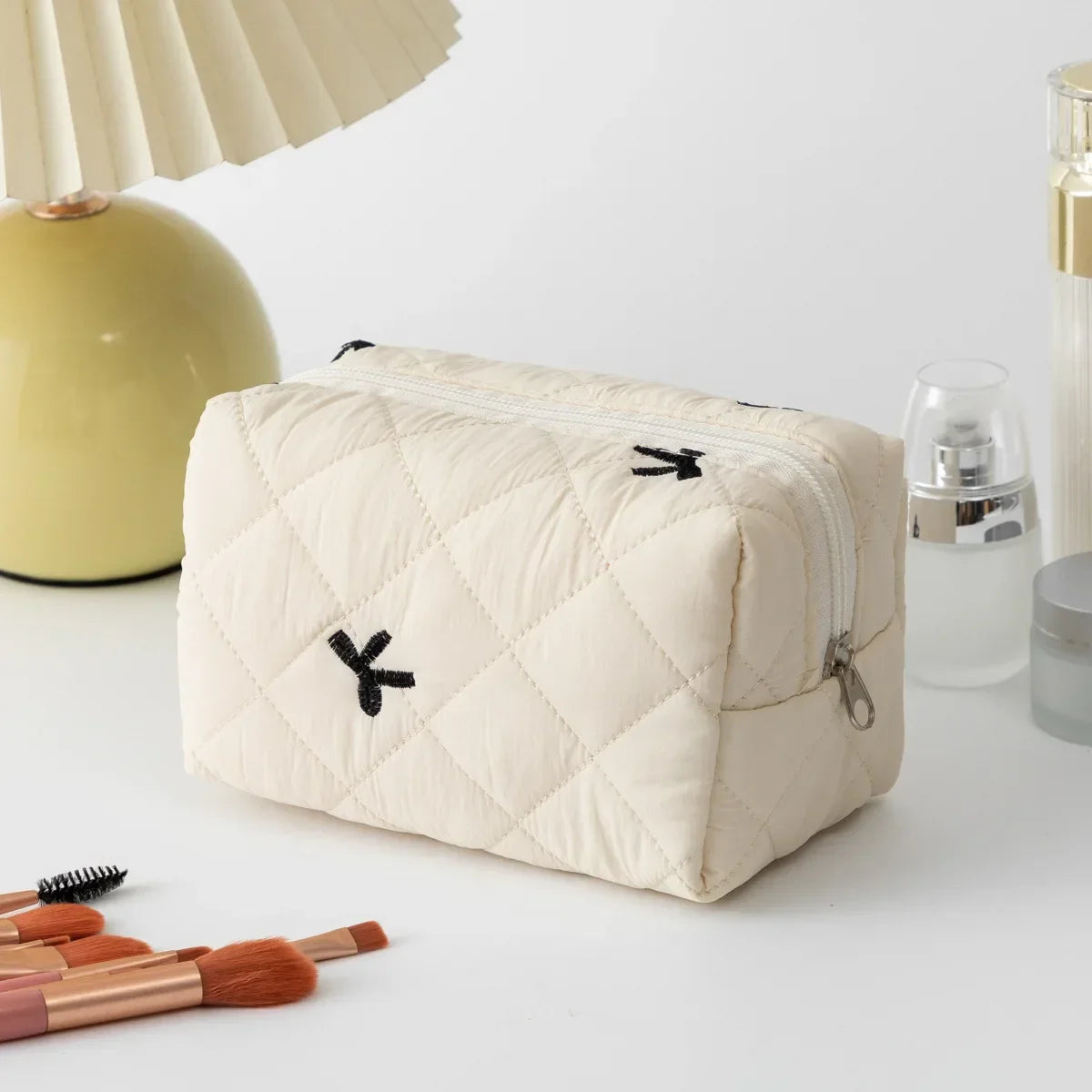 Cream quilted cosmetic bag with black bow embroidery and zip closure