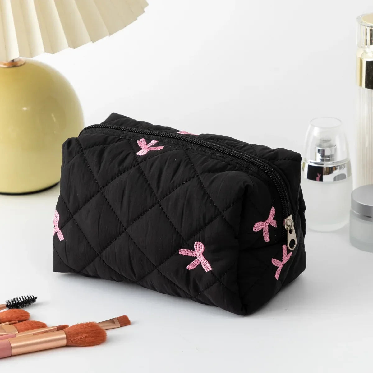 Black quilted cosmetic bag with pink bow embroidery and zip closure