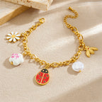 Gold-tone charm bracelet with ladybug pendant, white flower charm, and pearl drop accents