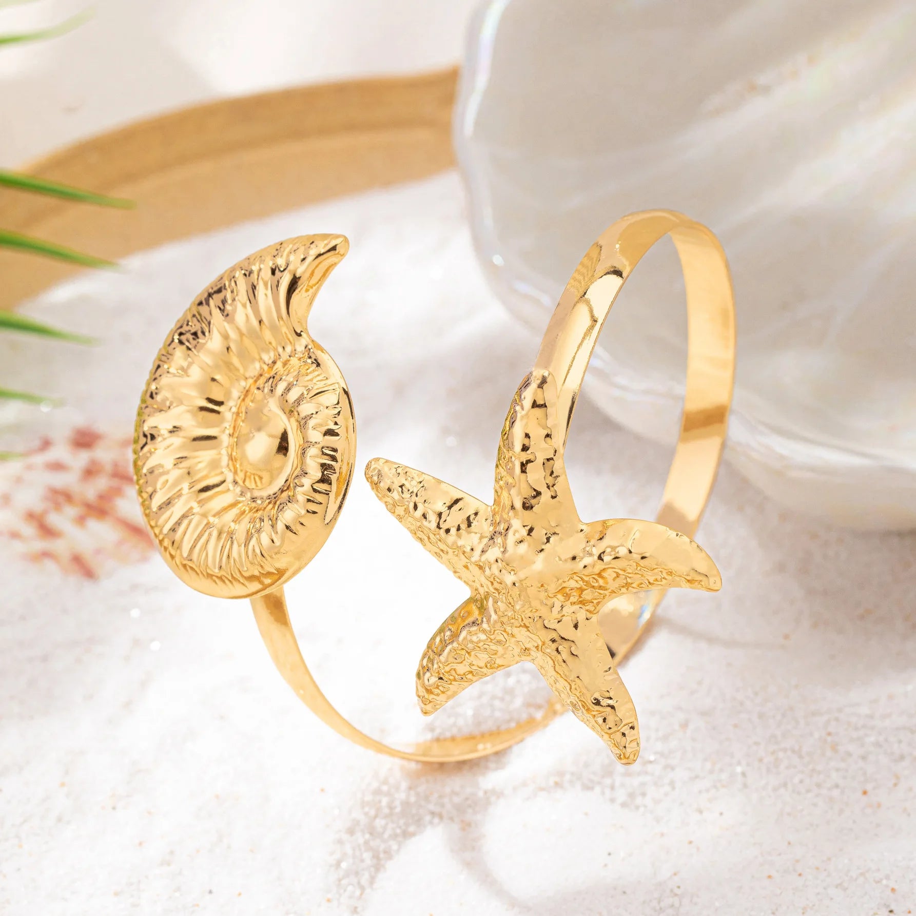 Gold shell-and-starfish arm cuff with raised round shell disk and textured starfish motif