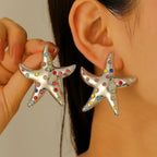 Silver starfish stud earrings with rainbow rhinestones, worn on ears