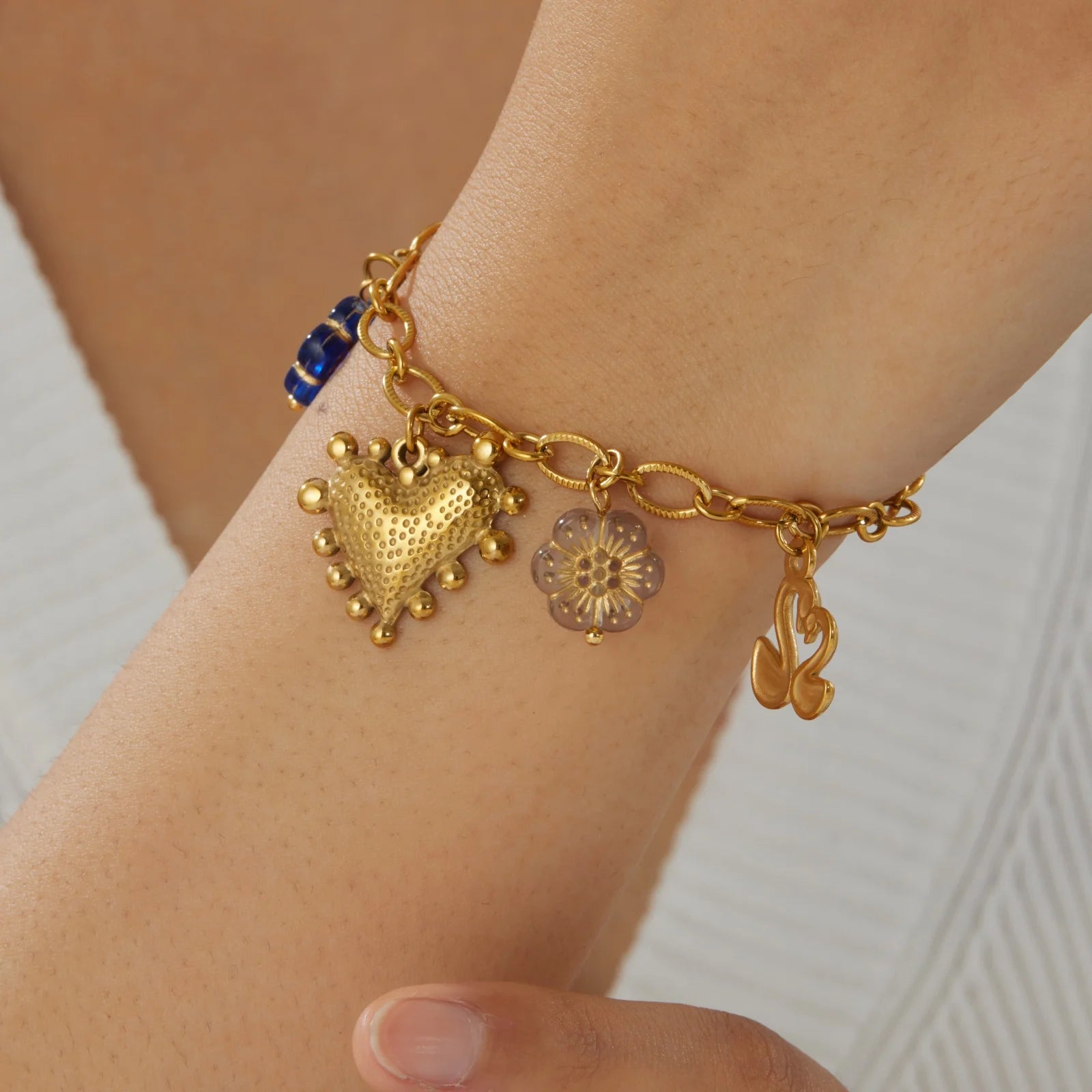 Gold-tone charm bracelet with blue accent heart charm, small flower charm, and bow charm