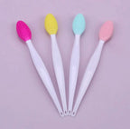 Five silicone cleansing brushes with white handles and colorful oval bristle heads