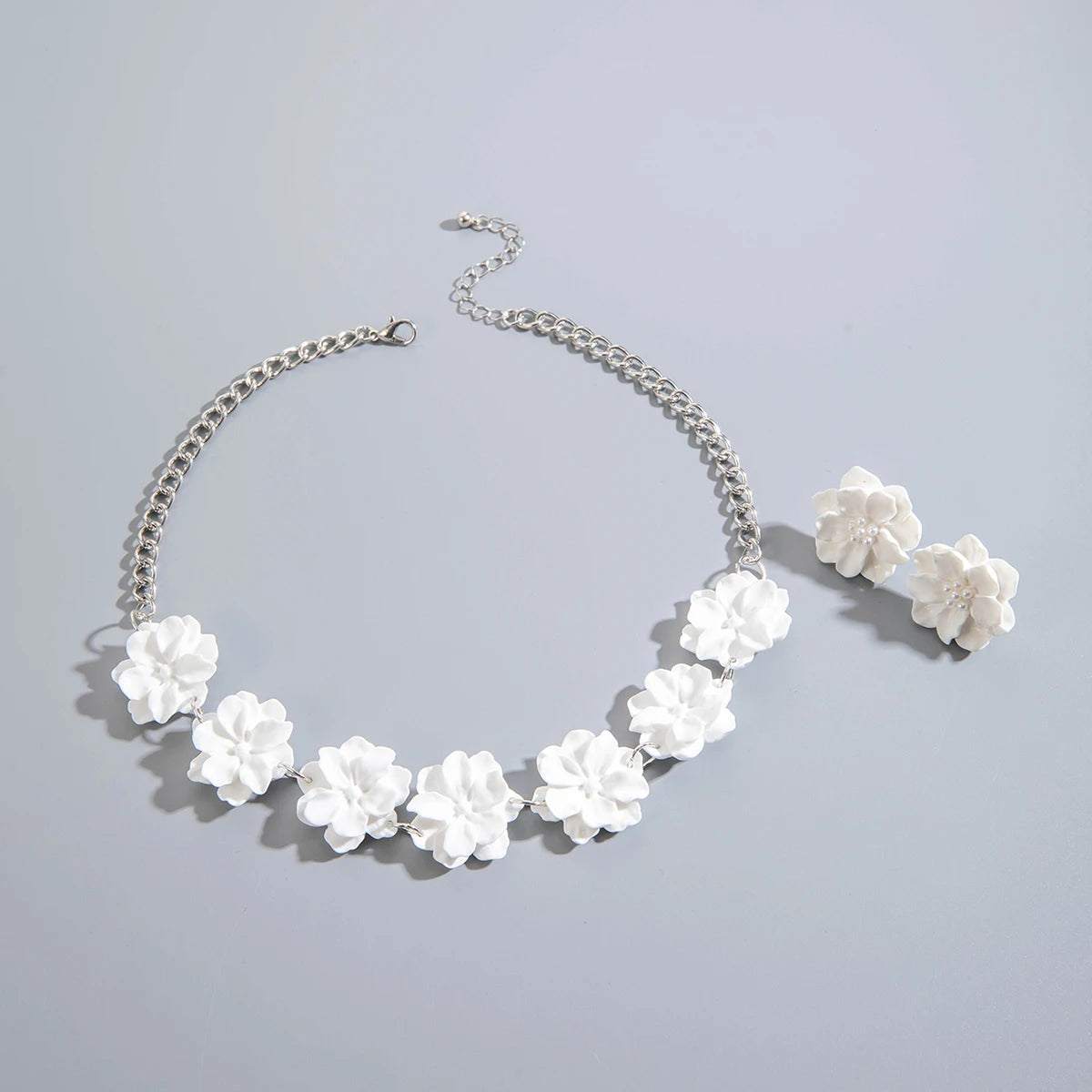 White flower necklace with silver-tone chain and matching stud earrings, flat lay