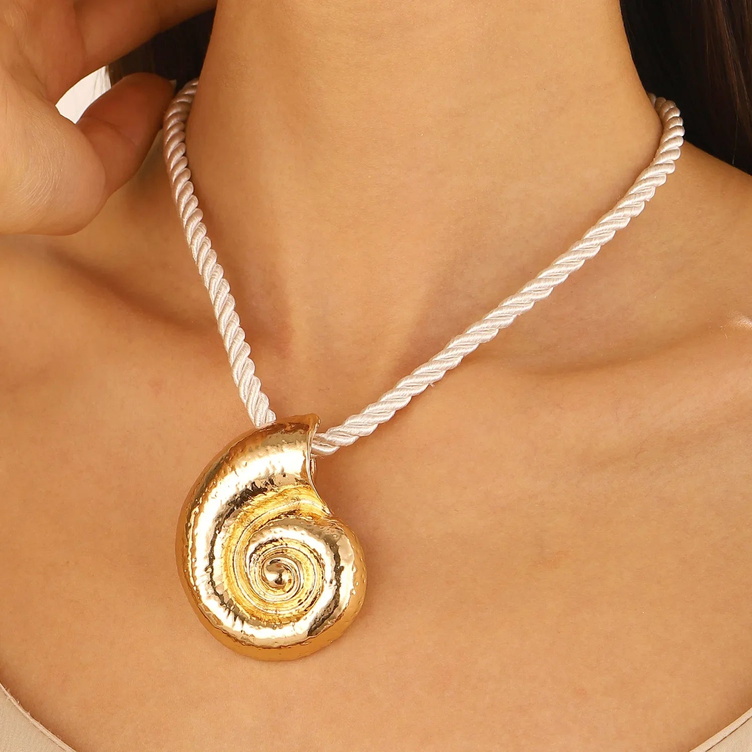 Gold conch shell pendant on white rope necklace cord, spiral swirl detail.