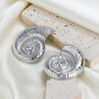 Silver conch shell stud earrings with spiral center, textured shell ridges.