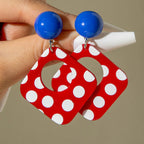 Red polka-dot geometric drop earrings with blue ball tops and curved cutout details