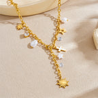 Gold-tone charm necklace with cross, stars, sun pendant, and white pearl beads