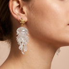 Gold starfish drop earrings with clear translucent jellyfish charms on ear.