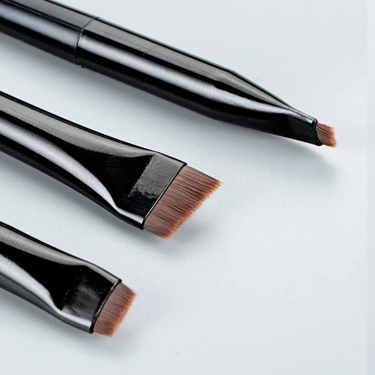 Eyeliner and eyebrow makeup brush tips, angled brown bristles on black handles