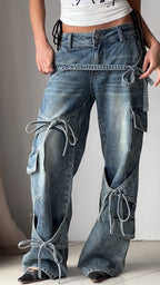 Blue denim utility jeans with long side straps, patch pockets, and knot ties at seams.