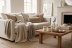 Beige sofa with multiple pillows and knit throw blanket, coffee table with candles