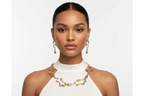 Gold-tone chain necklace and hoop earrings on model face, white sleeveless top.