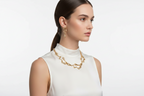 Gold-tone layered chain necklace and dangling earrings on model, white sleeveless top.