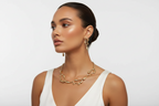 Gold-tone chain necklace and dangling earrings on model profile, white sleeveless top.
